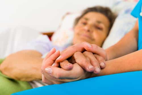 Caring nurse holding kind elderly lady's hands in bed.